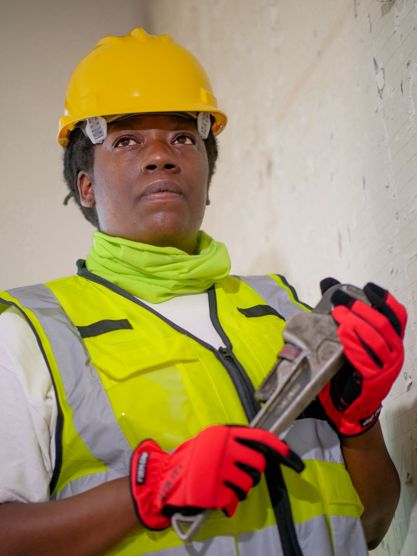 Plumber in a hard hat and safety vest holding a pipe wrench